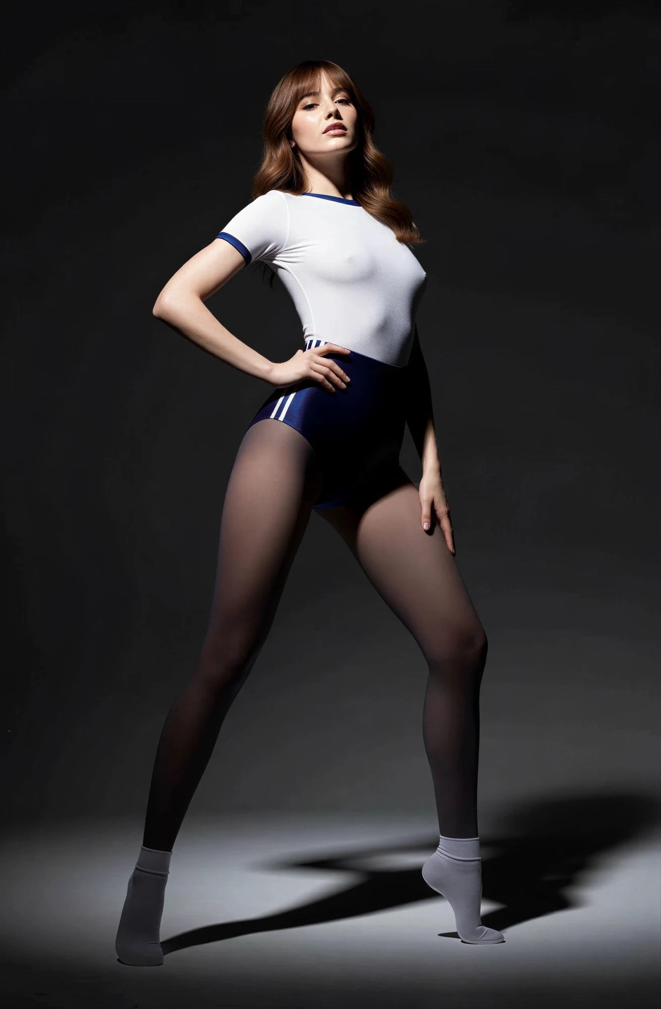 Person wearing a white top and black shorts with sheer stockings on a dark background