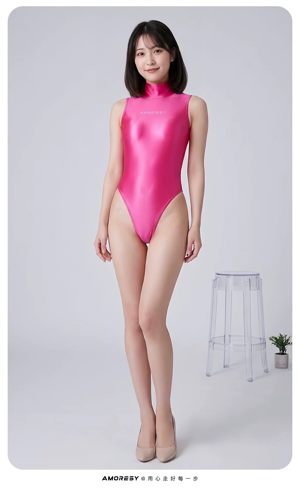 A woman modeling a shiny, high-neck, sleeveless bright pink bodysuit in a studio setting with a light gray background and a small clear stool.